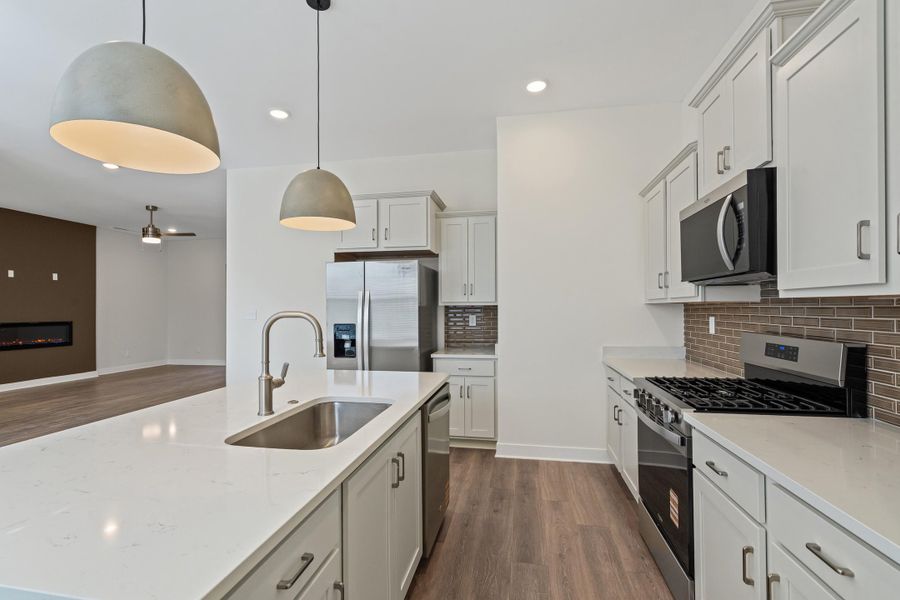 Kitchen featuring stainless steel appliances, dark wood-type flooring, hanging light fixtures, light stone countertops, and a kitchen island with sink