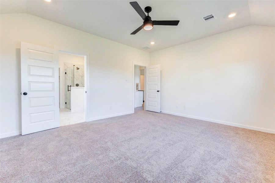 Spacious primary suite with plush carpeting, ceiling fan, and room for large furniture.
