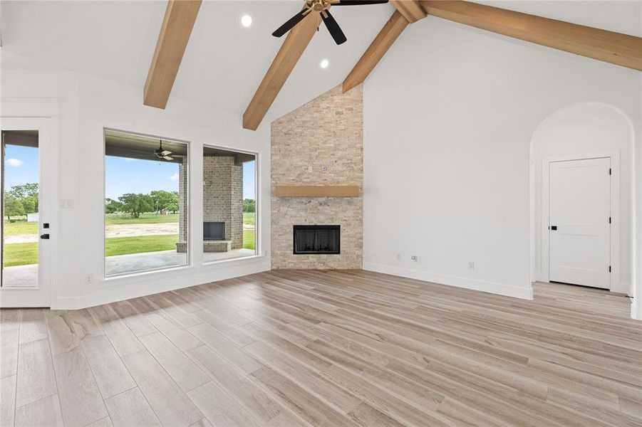 Unfurnished living room with high vaulted ceiling, a fireplace, beam ceiling, ceiling fan, and light wood-style flooring Unfurnished living room with high vaulted ceiling, a fireplace, beam ceiling, ceiling fan, and light wood-style flooring