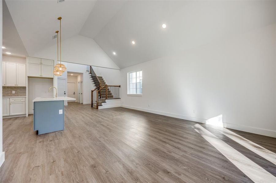 Unfurnished living room with light hardwood / wood-style floors, high vaulted ceiling, and sink