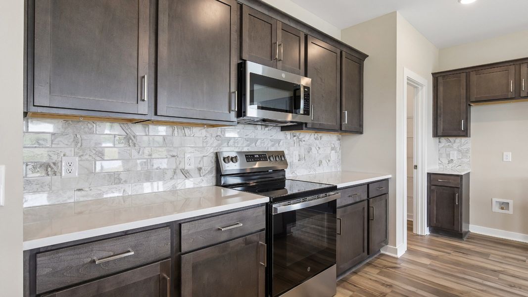 Kitchen with dark cabinetry, quartz countertops, stainless steel appliances, and tile backsplash