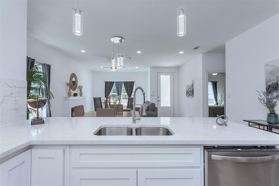 Kitchen featuring white cabinets, light stone countertops, dishwasher, decorative light fixtures, and sink