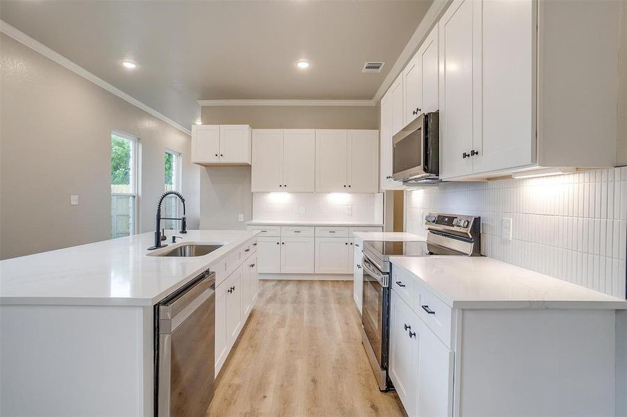 Kitchen with ornamental molding, a sink, light wood finished floors, backsplash, and stainless steel appliances Kitchen with ornamental molding, a sink, light wood finished floors, backsplash, and stainless steel appliances
