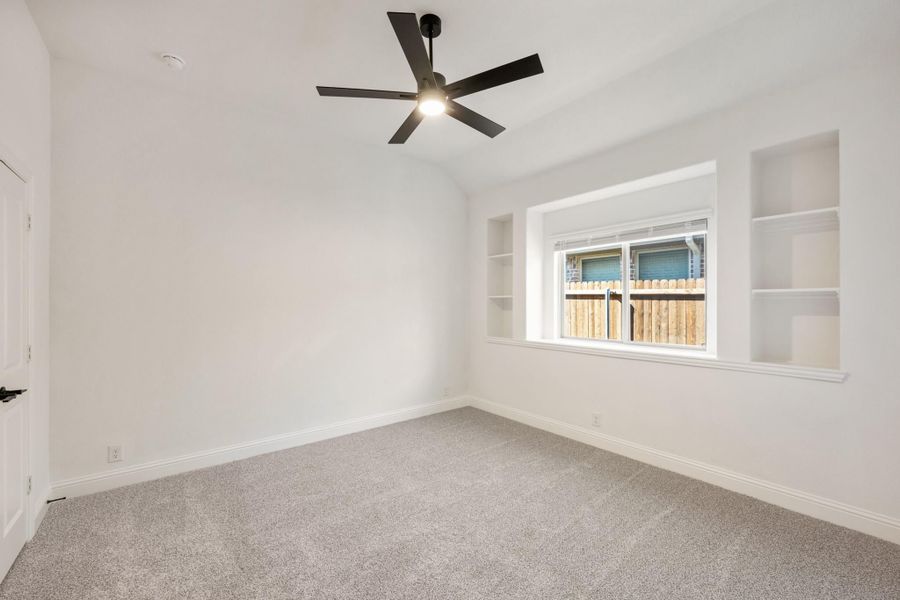Empty bedroom with vaulted ceiling, black ceiling fan, built-in shelves, and gray carpet Empty bedroom with vaulted ceiling, black ceiling fan, built-in shelves, and gray carpet