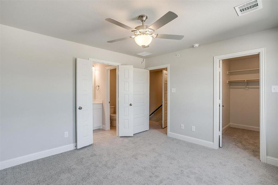Unfurnished bedroom featuring light carpet, a walk in closet, ensuite bathroom, and ceiling fan