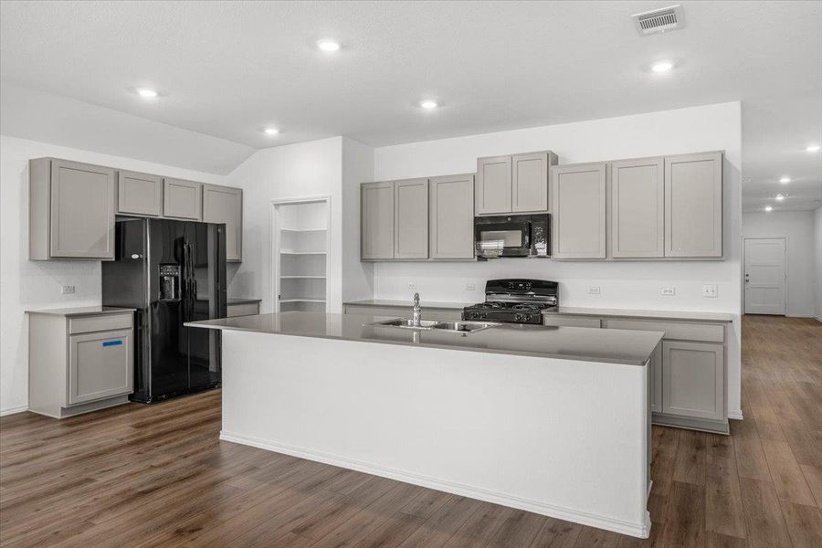 Kitchen with gray cabinets, black appliances, a kitchen island with sink, recessed lighting, and vaulted ceiling