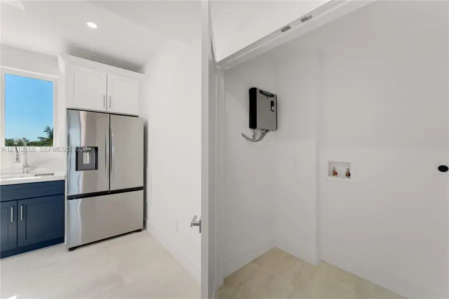 Stainless steel french-door refrigerator, dark navy cabinetry, white upper cabinetry, recessed lighting, and designated utility area with plumbing hookups Stainless steel french-door refrigerator, dark navy cabinetry, white upper cabinetry, recessed lighting, and designated utility area with plumbing hookups
