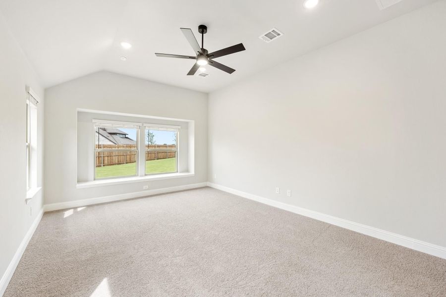 Empty bedroom with vaulted ceiling, ceiling fan, carpet flooring, and backyard-facing window Empty bedroom with vaulted ceiling, ceiling fan, carpet flooring, and backyard-facing window