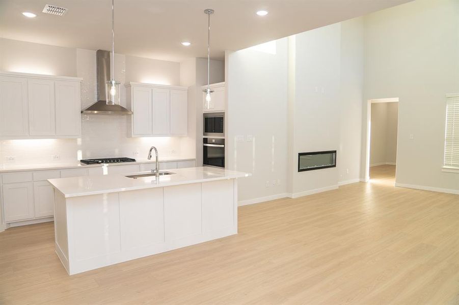 Open-concept living area featuring a modern kitchen with a large island, white cabinetry, stainless steel appliances, and wood-finish flooring Open-concept living area featuring a modern kitchen with a large island, white cabinetry, stainless steel appliances, and wood-finish flooring