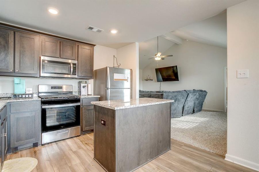 Kitchen featuring appliances with stainless steel finishes, a kitchen island, light wood-style floors, open floor plan, and dark brown cabinets