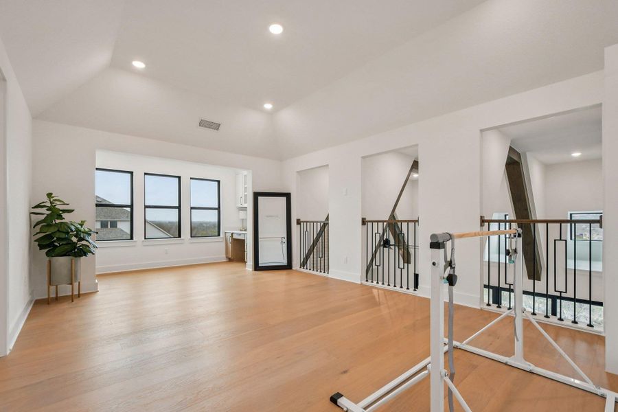 Versatile open space featuring hardwood flooring, a vaulted ceiling with recessed lighting, and a wall of three large windows providing ample natural light Versatile open space featuring hardwood flooring, a vaulted ceiling with recessed lighting, and a wall of three large windows providing ample natural light