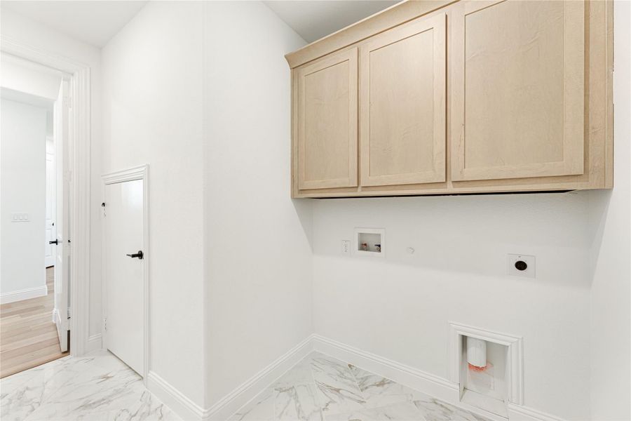 Laundry room with light wood upper cabinets, washer and dryer hookups, and marble tile flooring Laundry room with light wood upper cabinets, washer and dryer hookups, and marble tile flooring