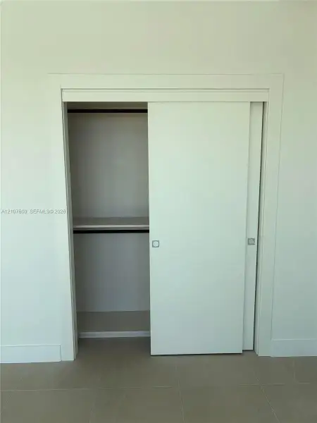 Minimalist closet featuring clean-lined sliding doors, integrated shelf, interior hanging rod, and recessed metal pulls