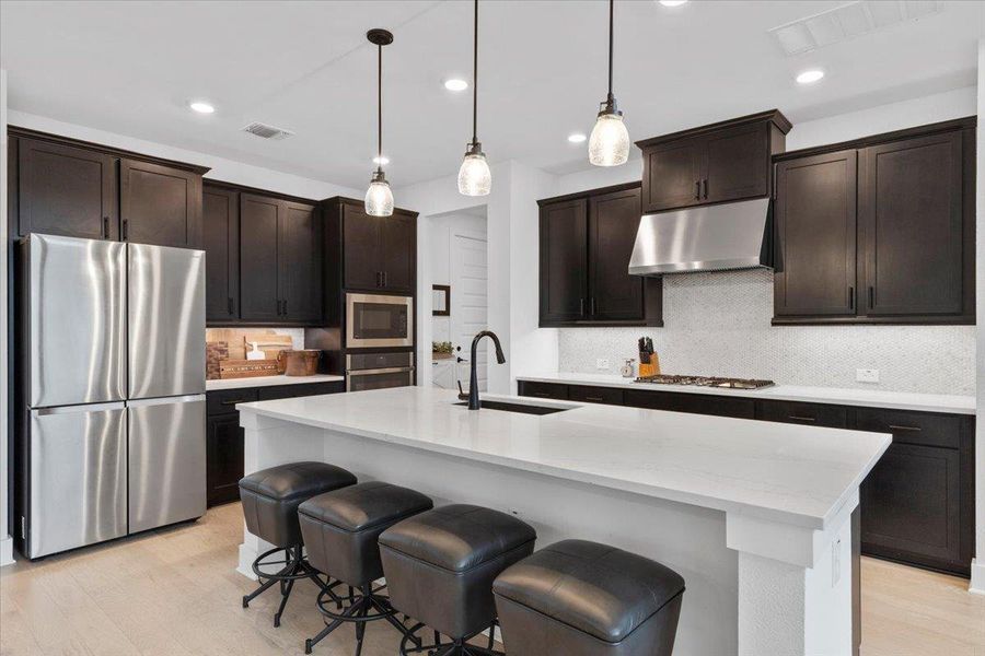 Kitchen featuring appliances with stainless steel finishes, under cabinet range hood, decorative backsplash, light wood-type flooring, and decorative light fixtures