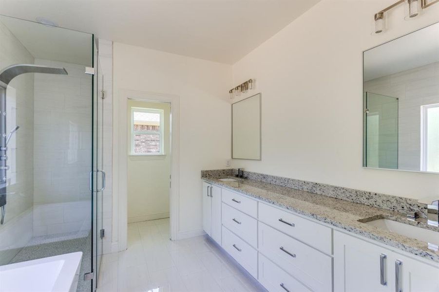 Full bathroom featuring double vanity, a stall shower, a tub, and baseboards