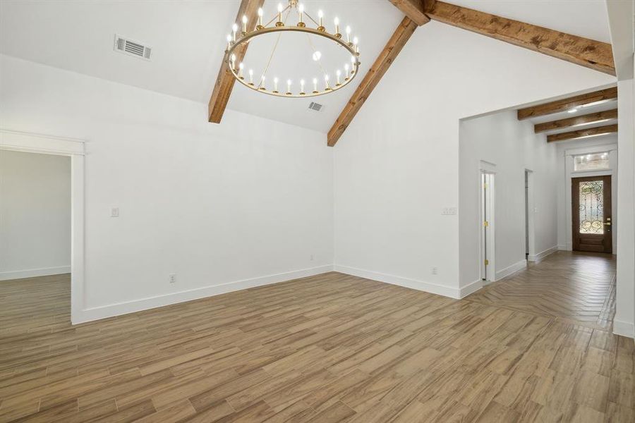 Unfurnished living room with beam ceiling, hardwood / wood-style flooring, high vaulted ceiling, and a chandelier