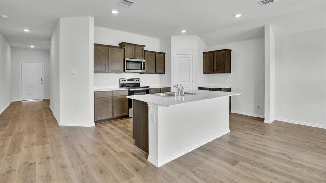 Kitchen featuring stainless steel appliances, an island with sink, dark wood finish cabinets, recessed lighting, and light wood-type flooring