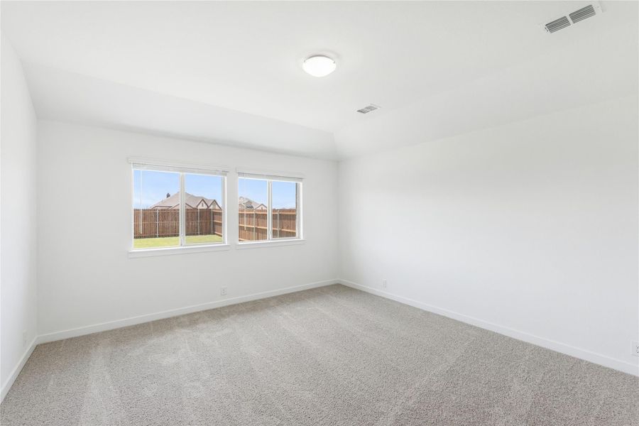 Empty bedroom with beige carpet, white walls, and a double window overlooking a fenced backyard