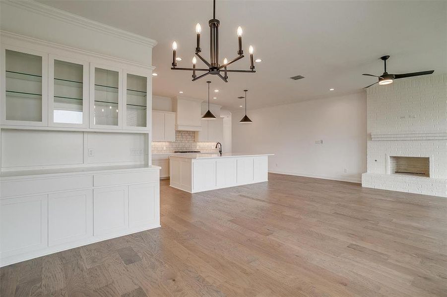 Unfurnished living room with a fireplace, ceiling fan with notable chandelier, crown molding, and light wood-type flooring