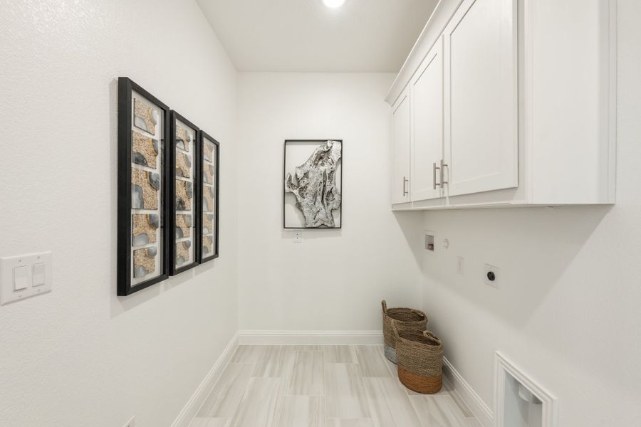 Laundry room with white upper cabinets, washer and dryer hookups, light wood floors, and woven baskets on the floor.