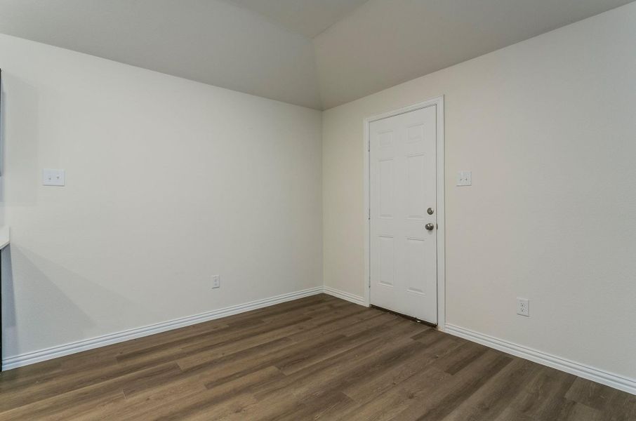 Spare room with vaulted ceiling, baseboards, and dark wood-type flooring