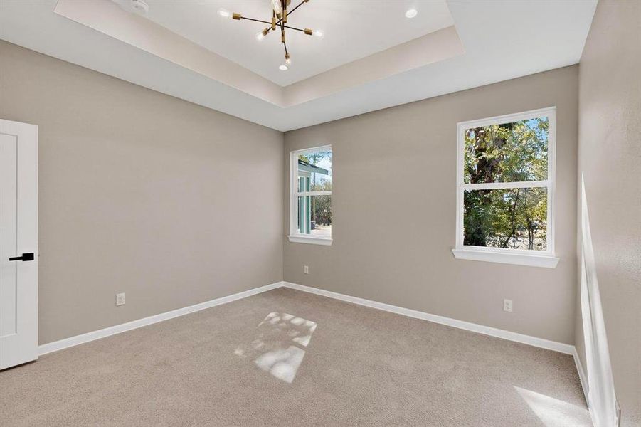 Empty room with light carpet, a chandelier, and a raised ceiling Empty room with light carpet, a chandelier, and a raised ceiling