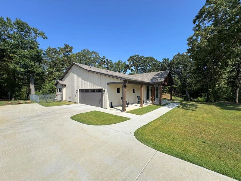 View of side of home with an attached garage, concrete driveway, a porch, a shingled roof, and view of scattered trees View of side of home with an attached garage, concrete driveway, a porch, a shingled roof, and view of scattered trees