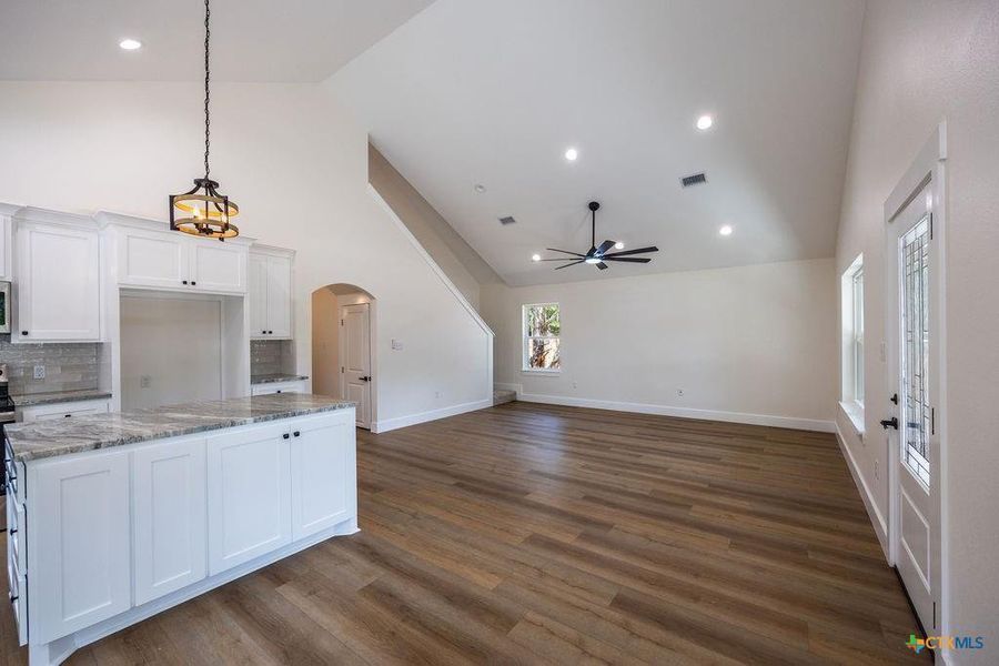 Kitchen with white cabinets, pendant lighting, arched walkways, a kitchen island, and light stone counters