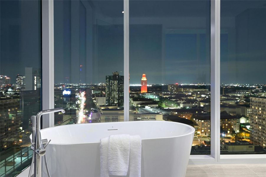 Spa-inspired primary bathroom with a freestanding soaking tub set against floor-to-ceiling windows, offering dramatic skyline and University Tower views.