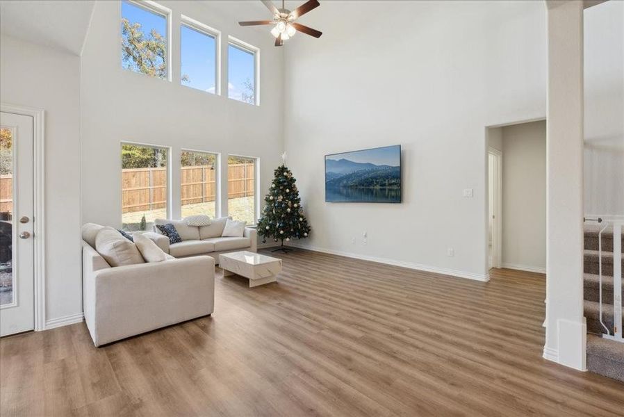 Living room with a high ceiling, light wood-type flooring, and ceiling fan