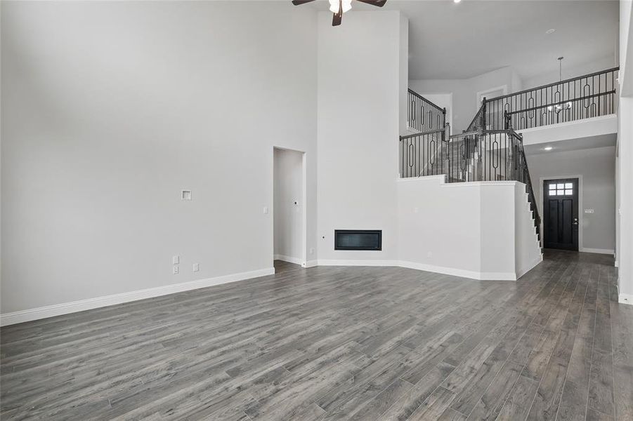 Unfurnished living room featuring a towering ceiling, dark wood-style floors, a ceiling fan, baseboards, and stairs Unfurnished living room featuring a towering ceiling, dark wood-style floors, a ceiling fan, baseboards, and stairs