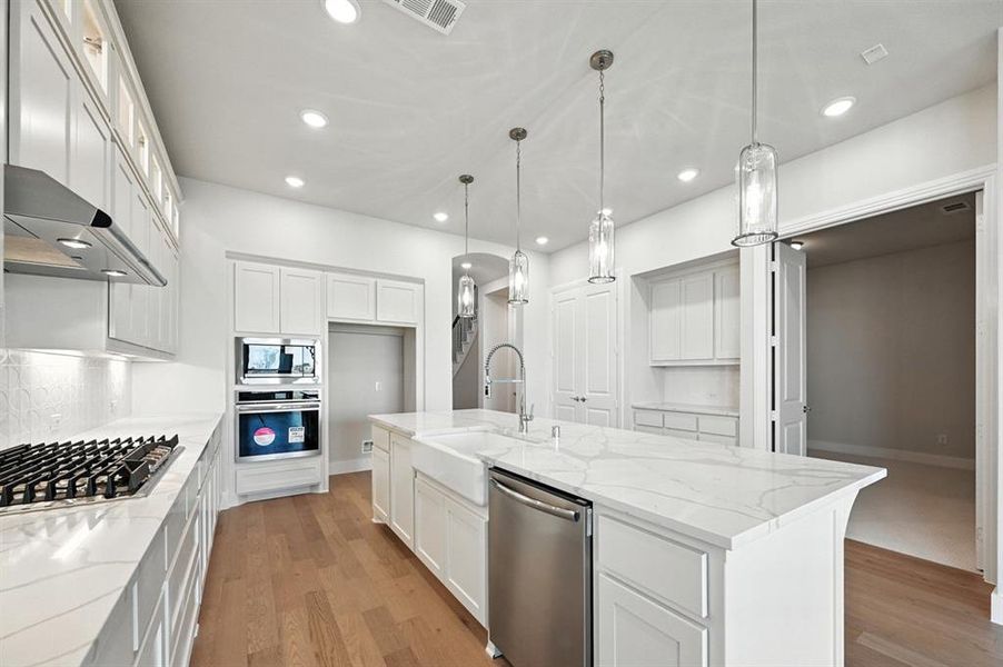 Kitchen with light stone countertops, light wood-style flooring, white cabinetry, appliances with stainless steel finishes, and recessed lighting Kitchen with light stone countertops, light wood-style flooring, white cabinetry, appliances with stainless steel finishes, and recessed lighting