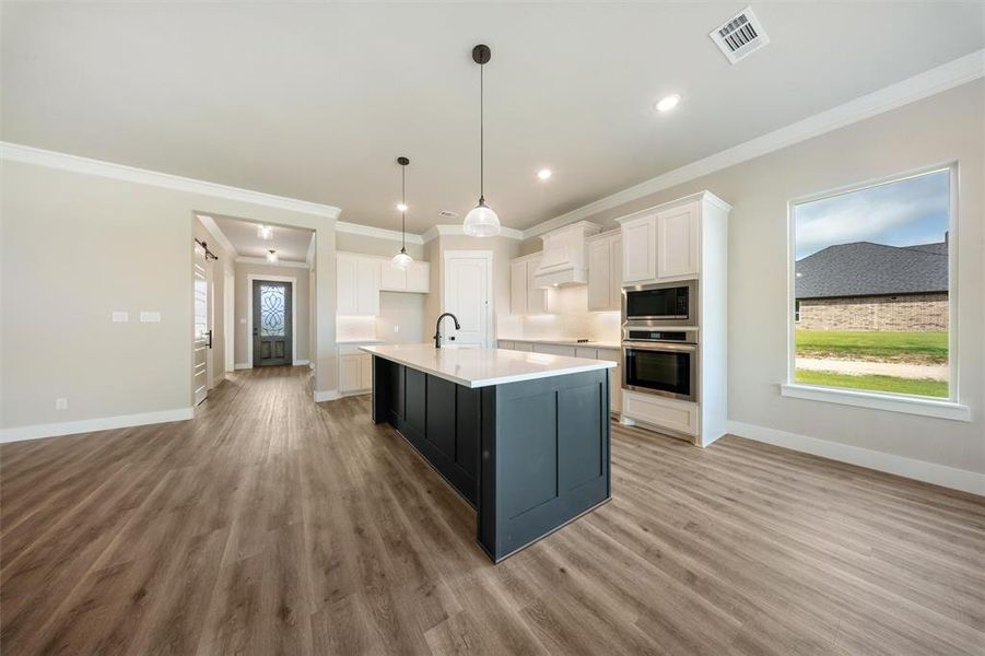 Kitchen with ornamental molding, white cabinetry, plenty of natural light, light wood-type flooring, and light countertops Kitchen with ornamental molding, white cabinetry, plenty of natural light, light wood-type flooring, and light countertops