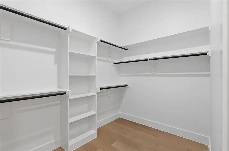 Walk-in closet featuring built-in shelving, multiple hanging rods, and wood-finish flooring Walk-in closet featuring built-in shelving, multiple hanging rods, and wood-finish flooring