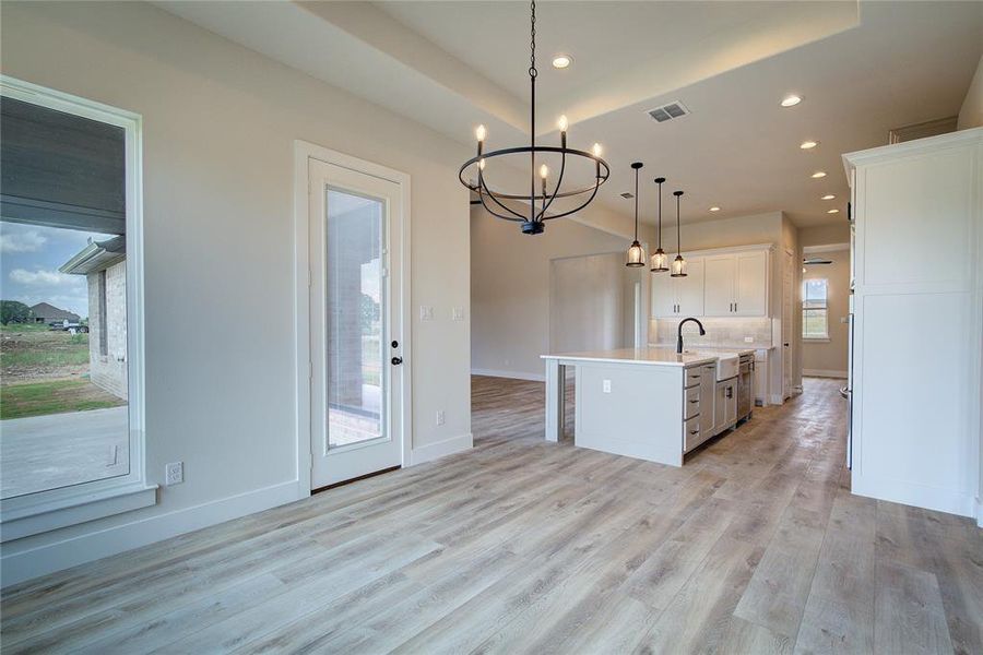 Kitchen featuring light hardwood / wood-style floors, white cabinetry, an island with sink, decorative light fixtures, and backsplash