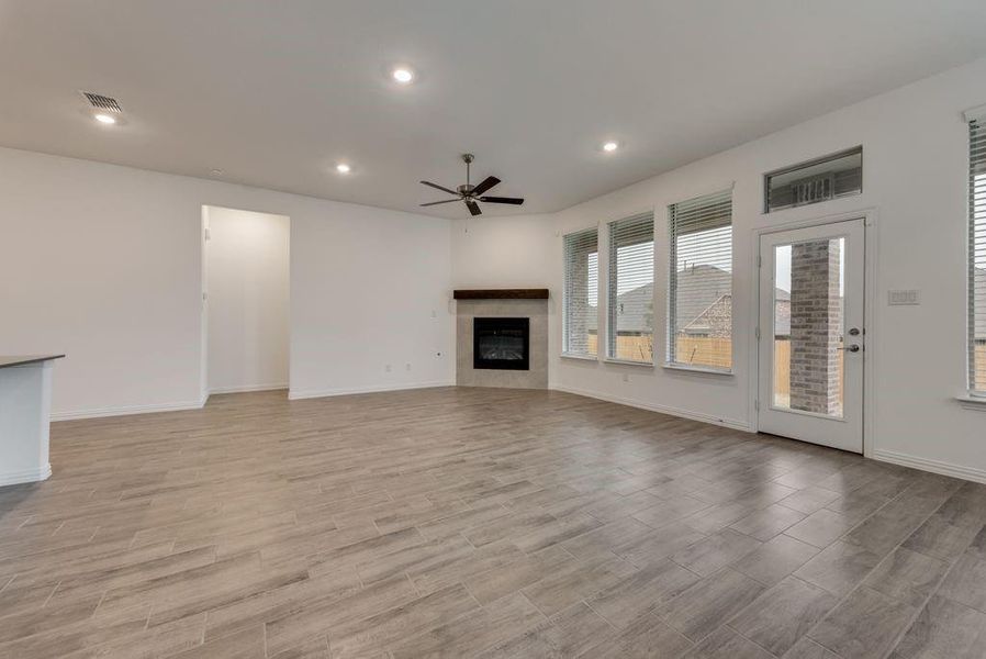 Unfurnished living room with ceiling fan, a tiled fireplace, and light hardwood / wood-style floors