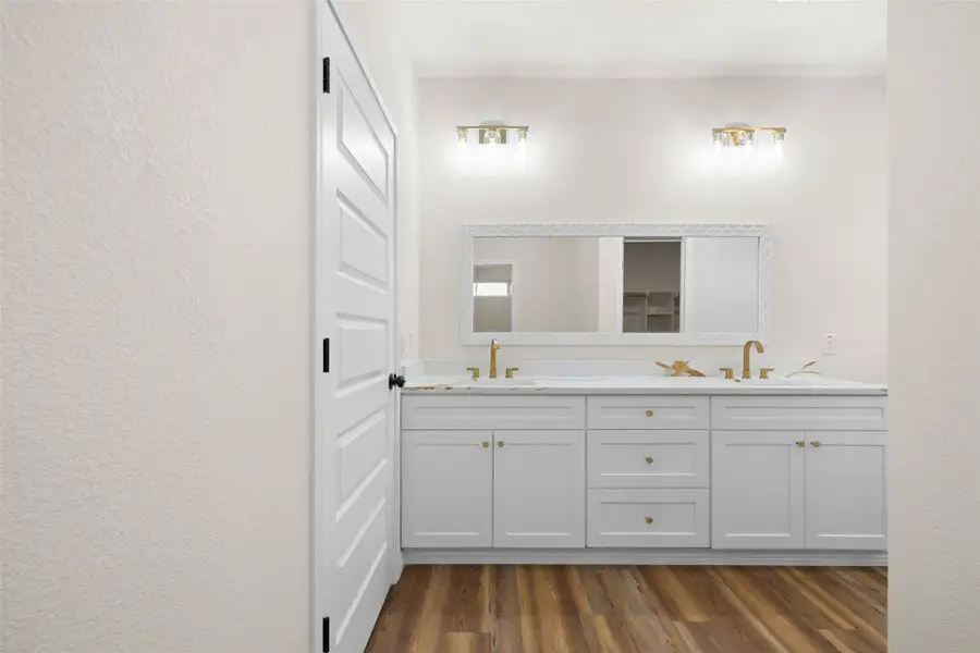 Full bathroom featuring a textured wall, double vanity, dark wood-style floors, and a closet Full bathroom featuring a textured wall, double vanity, dark wood-style floors, and a closet