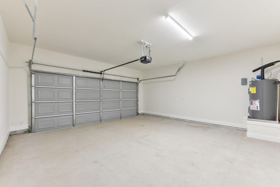 Garage featuring electric water heater, baseboards, and a garage door opener