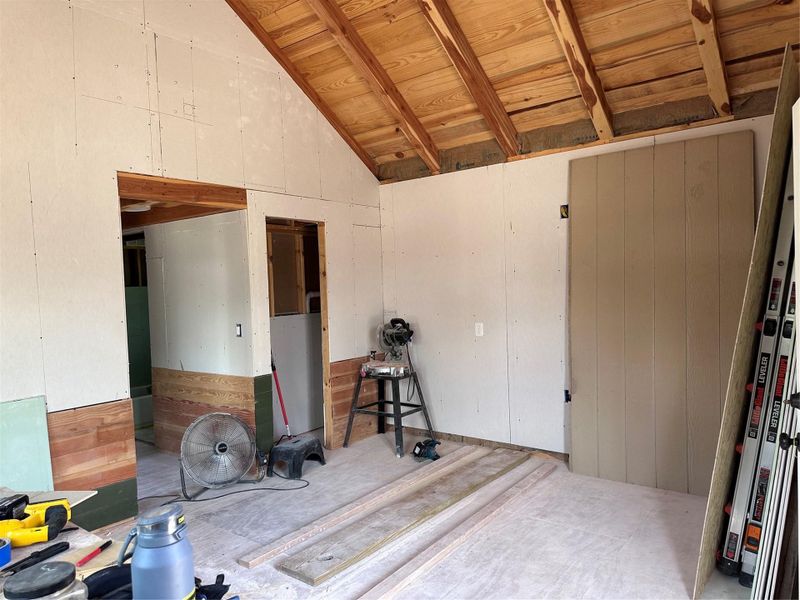 A spacious interior undergoing renovation, revealing exposed wooden ceiling beams and unfinished drywall.