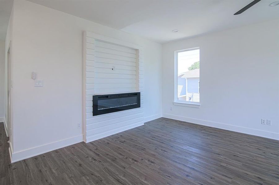 Unfurnished living room featuring ceiling fan, dark wood-type flooring, and a large fireplace