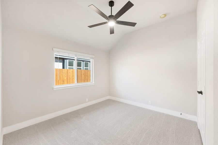 Empty bedroom with vaulted ceiling, black ceiling fan, carpet flooring, and a single window with backyard view.