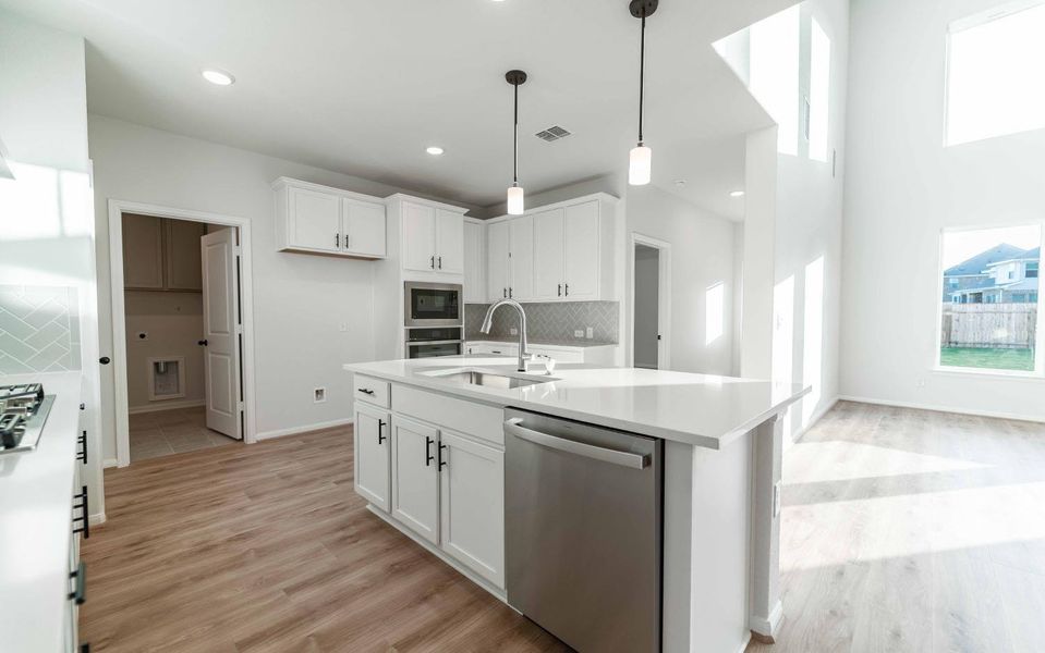 Kitchen featuring appliances with stainless steel finishes, pendant lighting, tasteful backsplash, white cabinetry, and light wood-style flooring