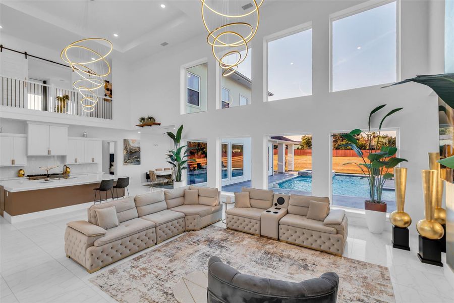 Great Room with Pool Views:Sink into comfort as oversized windows frame the sparkling pool and bathe the room in natural light. Over 20-foot ceilings and sculptural chandeliers crown the space, while the open flow to the kitchen and dining invites effortless entertaining. Imagine evenings here, light dancing across the water outside, laughter carrying through the home, and every gathering elevated by the elegance of design and the beauty of the view.