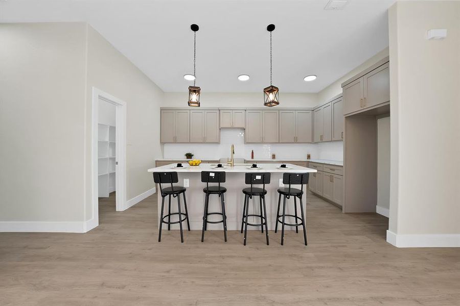 Kitchen with a kitchen breakfast bar, gray cabinets, pendant lighting, an island with sink, and light wood finished floors