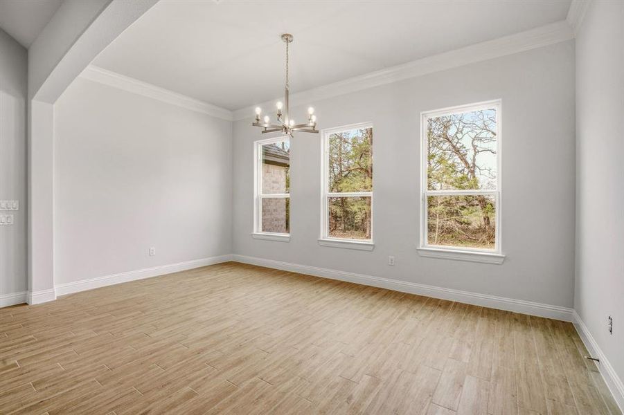 Empty room featuring crown molding, a chandelier, light wood-type flooring, and plenty of natural light Empty room featuring crown molding, a chandelier, light wood-type flooring, and plenty of natural light
