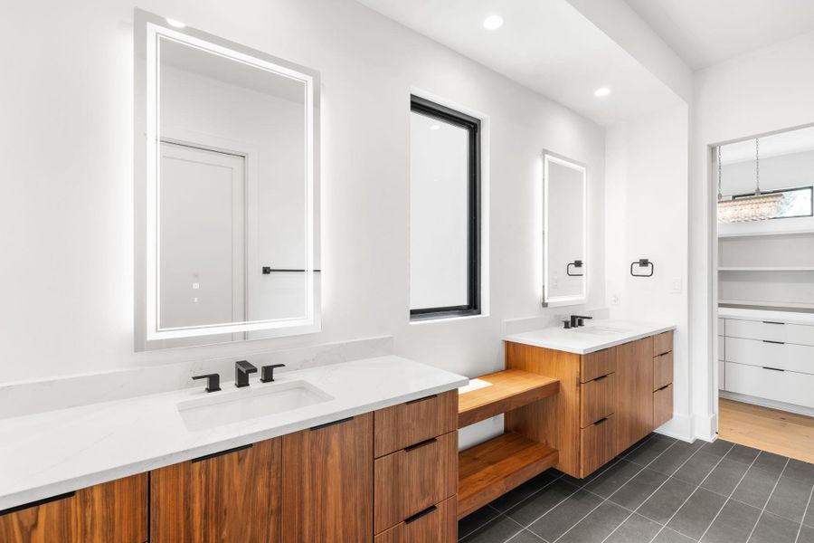 Dual vanities with illuminated mirrors and rich wood cabinetry create a sleek, contemporary bathroom oasis.