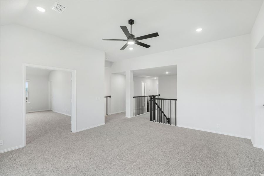 Open upstairs loft area with gray carpet, black ceiling fan, and staircase railing overlooking lower level Open upstairs loft area with gray carpet, black ceiling fan, and staircase railing overlooking lower level