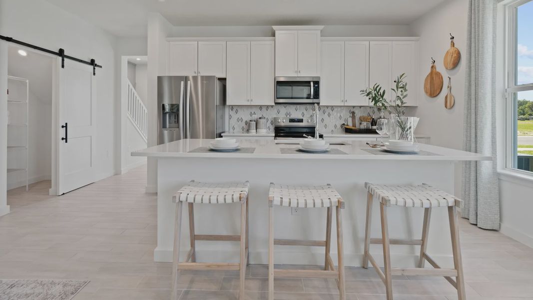 Open kitchen with white cabinets and large island at a DRB Homes Ambersweet model at the Trinity Place community. Open kitchen with white cabinets and large island at a DRB Homes Ambersweet model at the Trinity Place community.