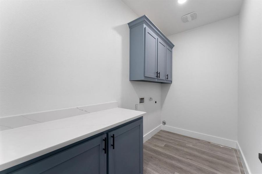 Clothes washing area with hookup for a washing machine, hookup for a gas dryer, light hardwood / wood-style flooring, and cabinets