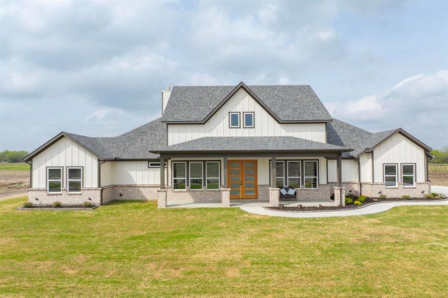 Modern inspired farmhouse with a shingled roof, french doors, brick siding, and a front yard Modern inspired farmhouse with a shingled roof, french doors, brick siding, and a front yard